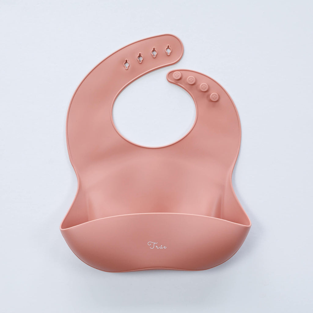A rosy mauve, BPA-free Silicone Bucket Bib with an adjustable neck strap featuring snap buttons. The bib has a scoop at the bottom to catch food.
