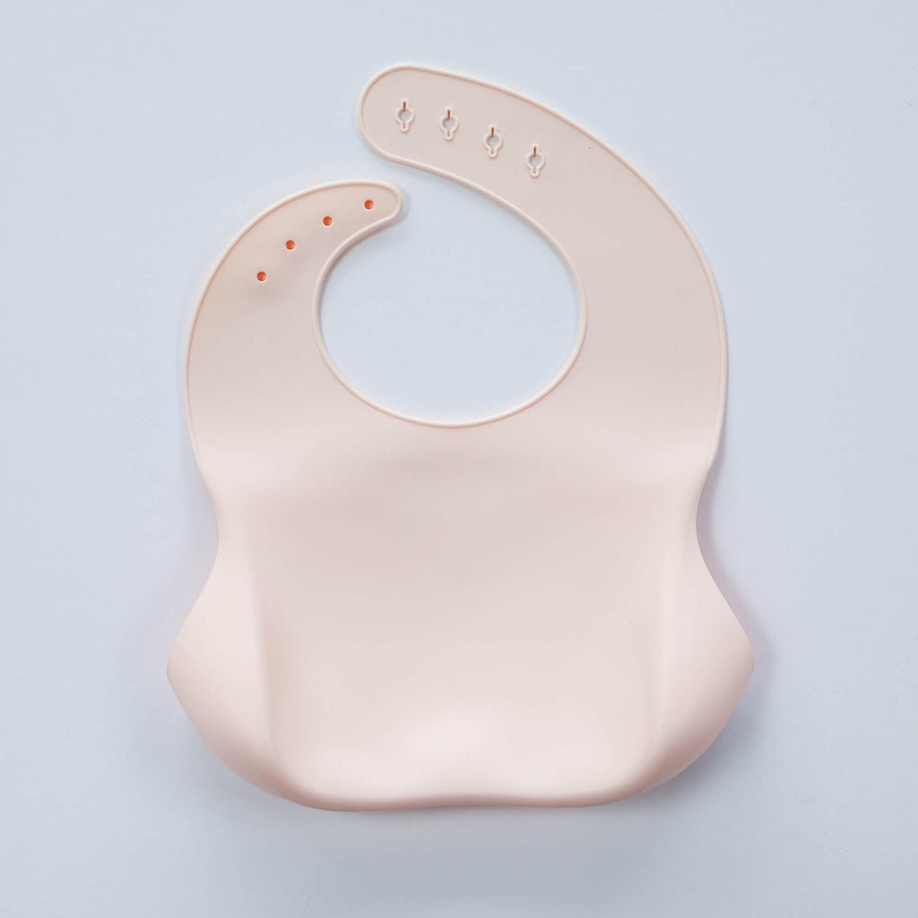 A pastel pink, BPA-free Silicone Bucket Bib with an adjustable neck strap featuring snap buttons. The bib has a scoop at the bottom to catch food.