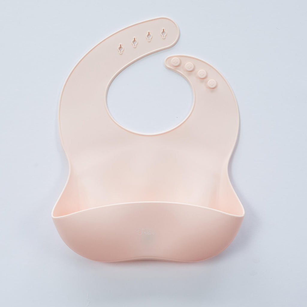 A pastel pink, BPA-free Silicone Bucket Bib with an adjustable neck strap featuring snap buttons. The bib has a scoop at the bottom to catch food.
