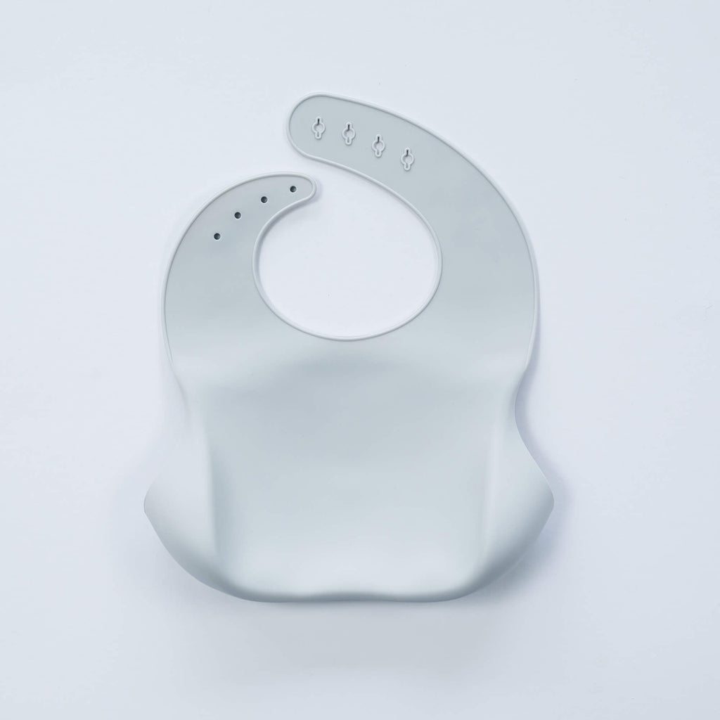 A white, BPA-free Silicone Bucket Bib with an adjustable neck strap featuring snap buttons. The bib has a scoop at the bottom to catch food.