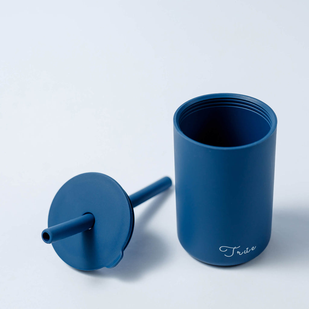 A cylindrical blue cup with a straw and a lid, featuring the word ‘True’ in a light font near the bottom.