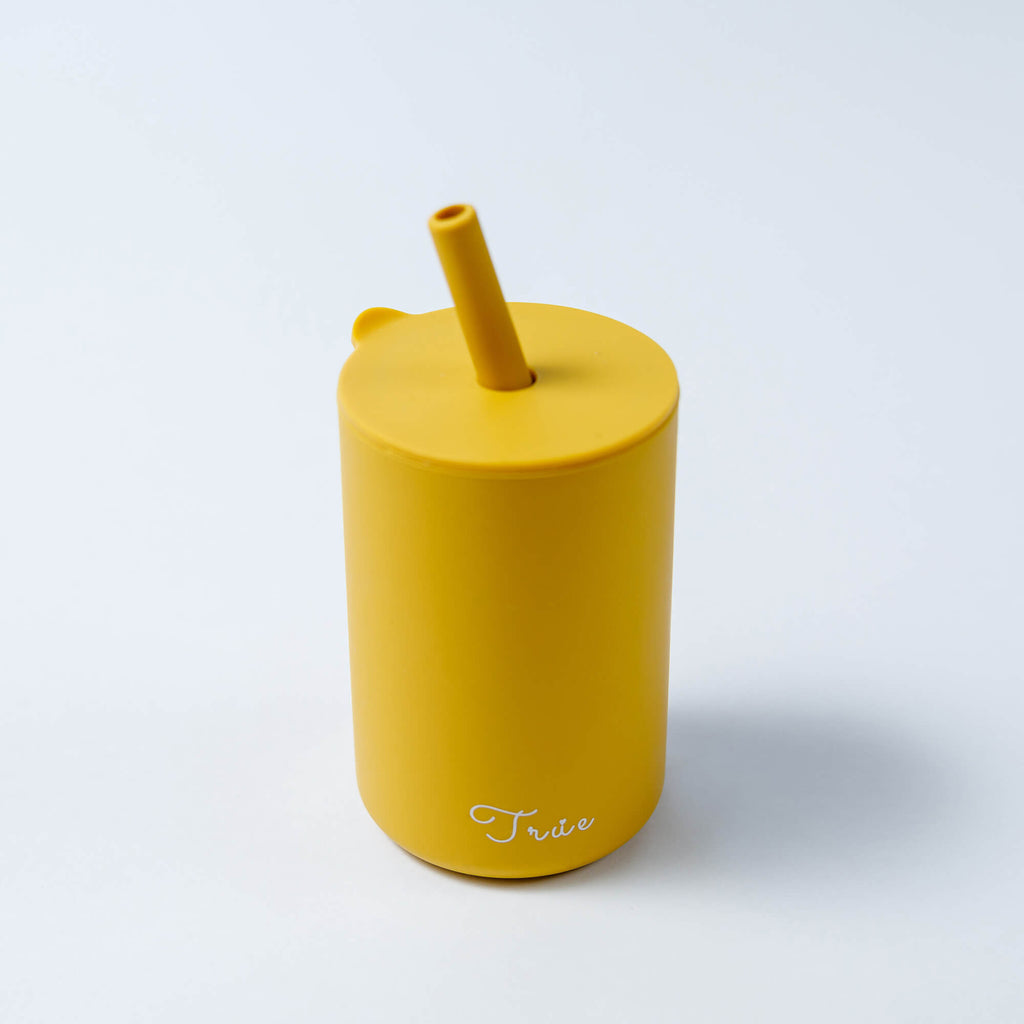 A cylindrical yellow cup with a straw and a lid, featuring the word ‘True’ in a light font near the bottom.