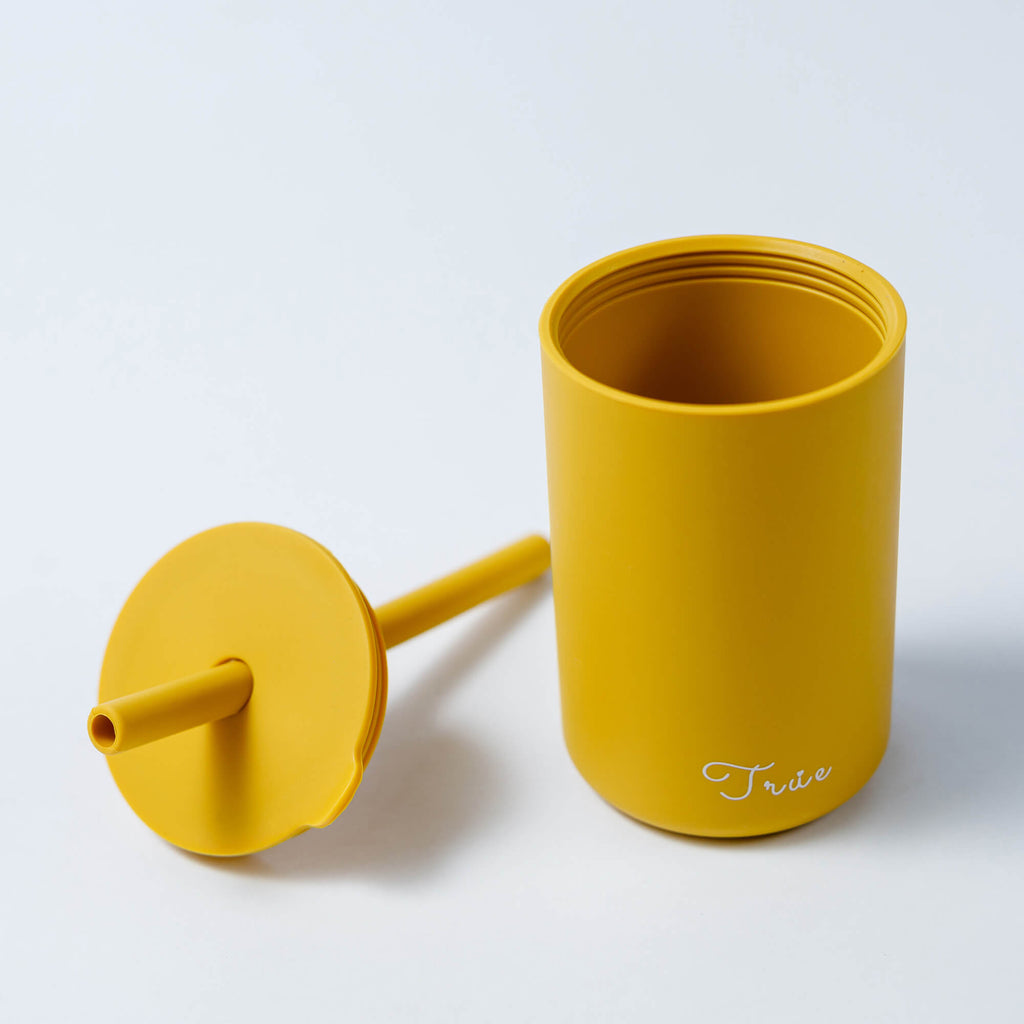 A cylindrical yellow cup with a straw and a lid, featuring the word ‘True’ in a light font near the bottom.