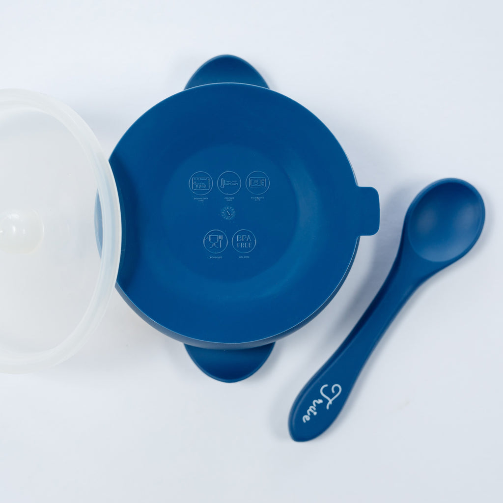 A midnight blue silicone suction bowl with two handles and a lid, including a spoon labeled with the brand ‘True'.