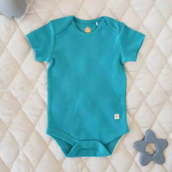 Teal baby onesie on a quilted surface with gray toys