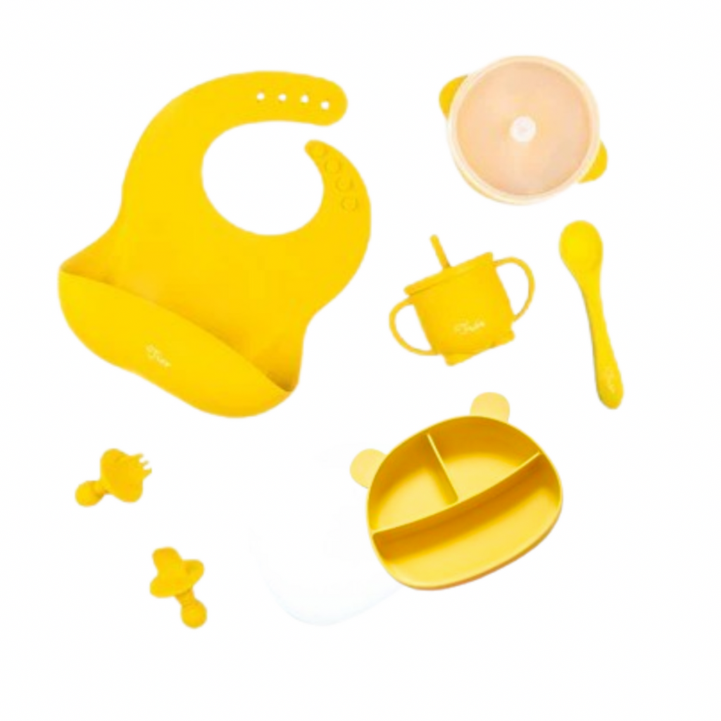 The Kids Tableware Set - Starter Luxe Bundle, featuring a range of five different color baby feeding items. These include a silicone bucket bib, a double handed silicone straw cup, set of toddlers' anti choke cutlery and a spoon, a suction bowl with a lid and a bear shaped divided plate with lid.