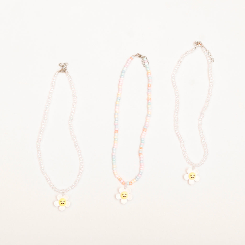 Three necklaces with smiley face charms on a light pink background