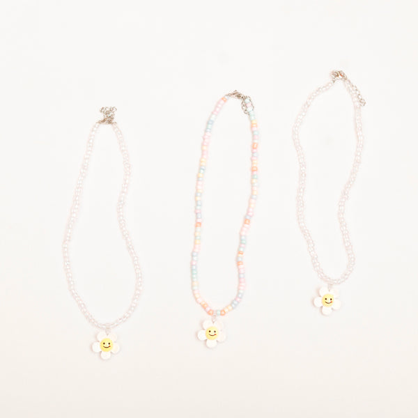 Three necklaces with smiley face charms on a light pink background