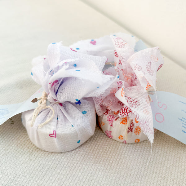Two wrapped baby soaps with multicolored patterns on the wrapping, placed on a light surface.