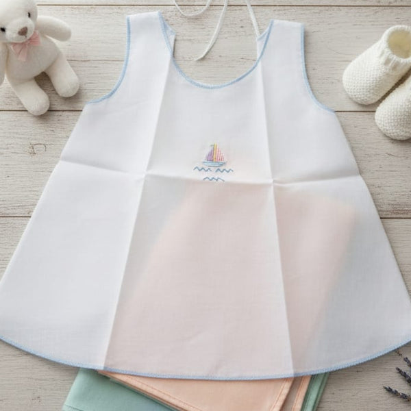 Set of baby bibs on a wooden surface with a teddy bear and booties in the background.