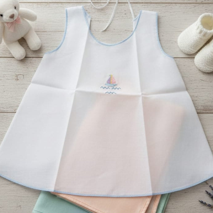 Set of baby bibs on a wooden surface with a teddy bear and booties in the background.