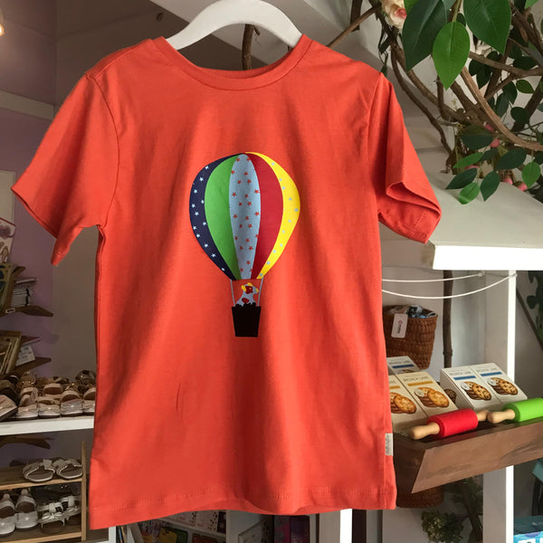 An orange t-shirt with a colorful balloon print hanging on a display rack.