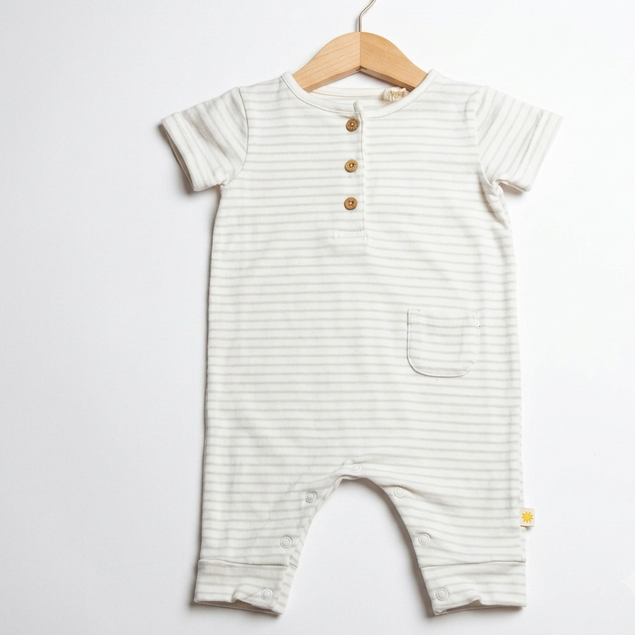 A baby romper with thin horizontal stripes in cream and light sage green, featuring a short button placket and a front pocket, hanging on a wooden hanger against a white background.