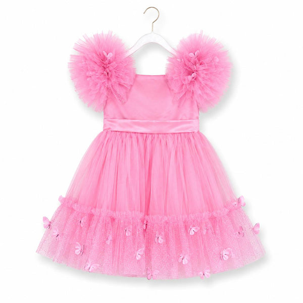 A pink toddler girl's party dress with a tiered tulle skirt and fluffy pom-pom shoulder details, hanging on a white plastic hanger against a white background.