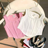 Pink and white tank tops on hangers with a chair and magazine in the background.