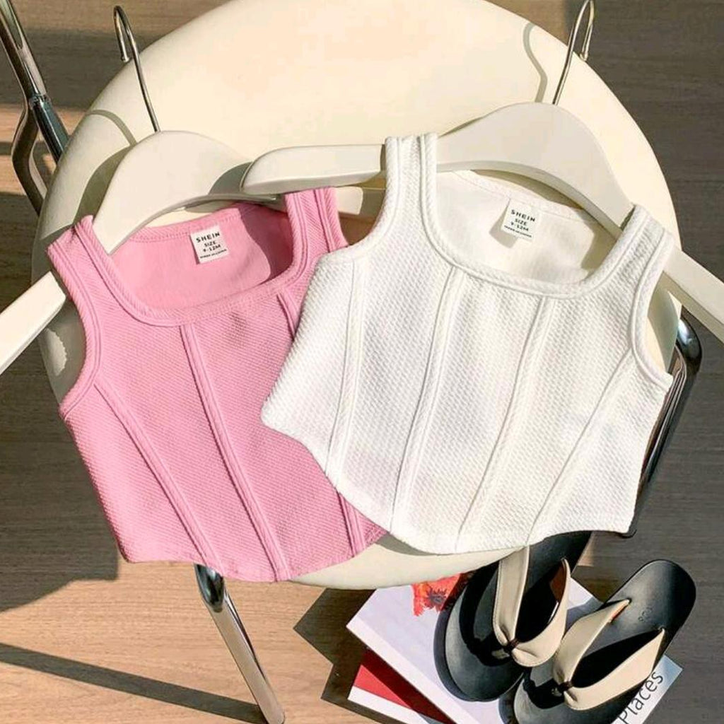 Pink and white tank tops on hangers with a chair and magazine in the background.
