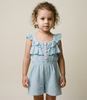 Child wearing a light blue ruffled romper against a beige background