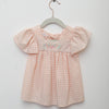 Pink checkered dress on a hanger against a light gray background