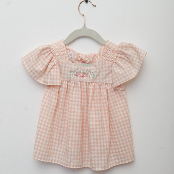 Pink checkered dress on a hanger against a light gray background