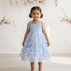 Young girl wearing a light blue floral dress against a white background with decorative flowers.