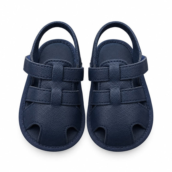 A pair of navy blue baby sandals with a pebbled leather texture, featuring cutout details and adjustable hook-and-loop straps, shown against a plain white background.