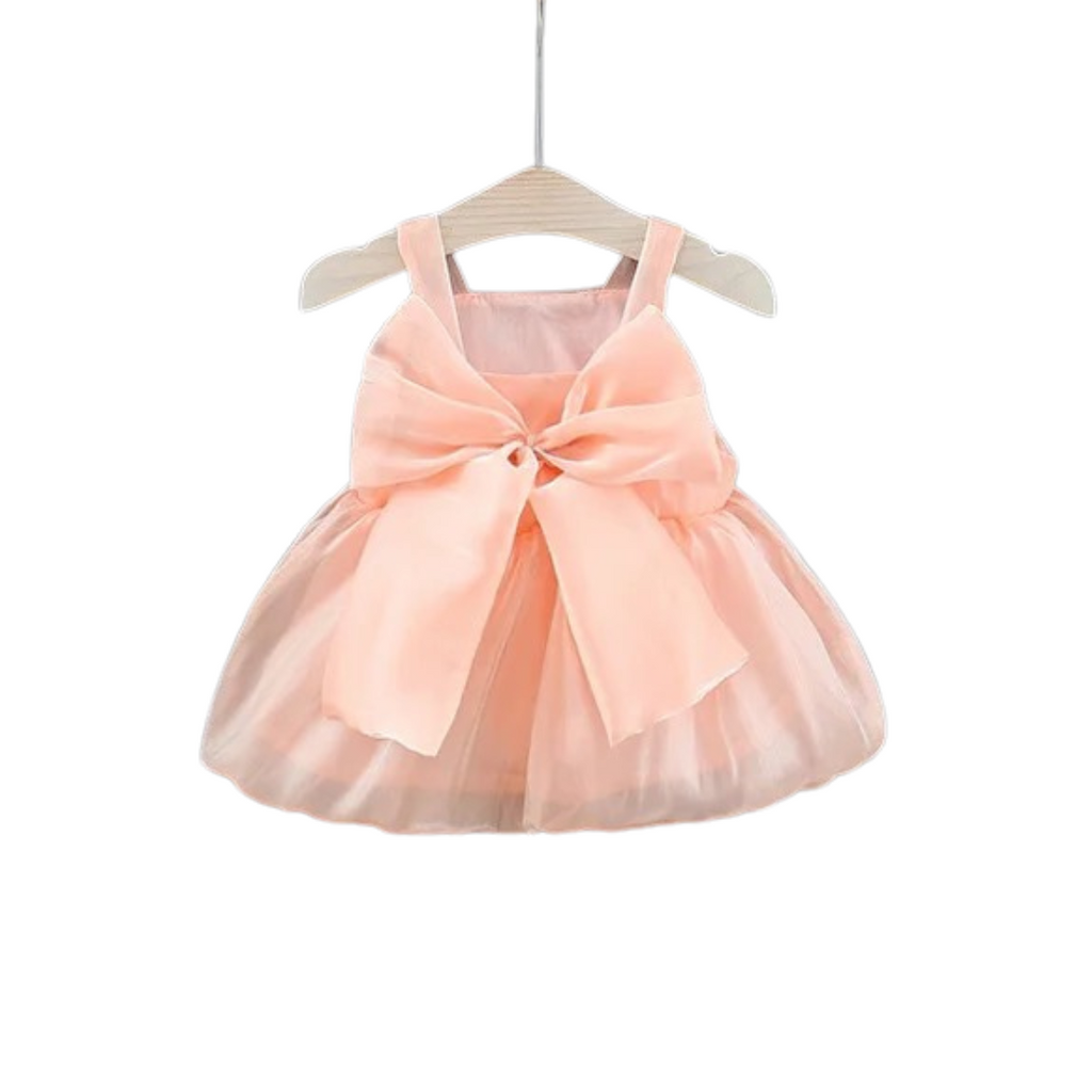 A peach-colored baby tulle party dress with a bow front on a hanger.