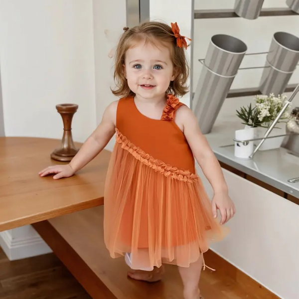 Young girl in an orange dress standing in a kitchen.