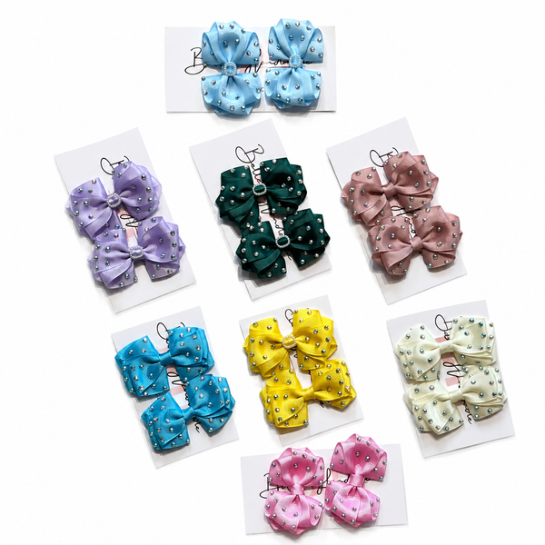 Nine pairs of small fabric hair bows in assorted pastel and bright colors, each with tiny white polka dots, displayed on white backing cards against a light gray background.