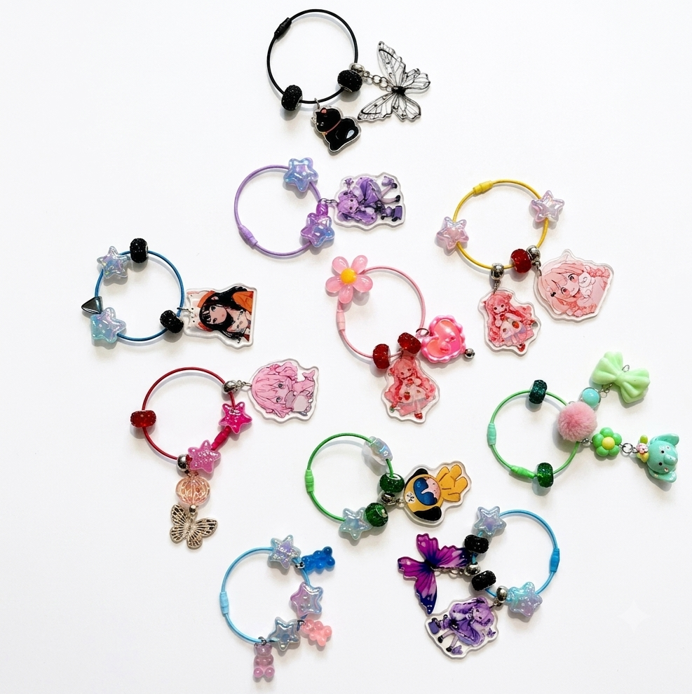 A collection of colorful hair claw clips arranged on a plain white background. The clips feature various charms including butterflies, flowers, hearts, cartoon characters, and pom-poms in a wide range of colors.