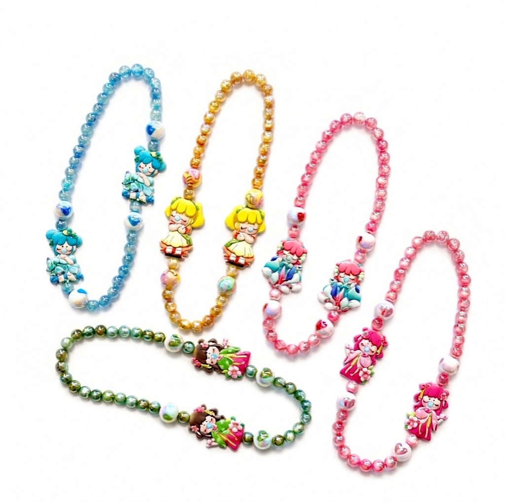 Four beaded character necklaces arranged on a white background, each with a different color scheme: blue, gold, pink, and green. The necklaces feature cartoon-style charms and heart-shaped beads.