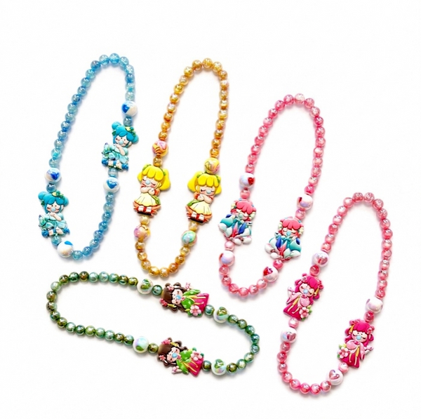 Four beaded character necklaces arranged on a white background, each with a different color scheme: blue, gold, pink, and green. The necklaces feature cartoon-style charms and heart-shaped beads.