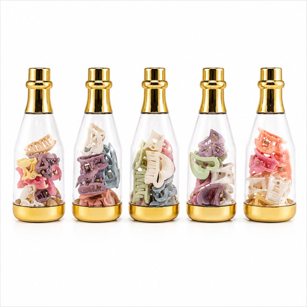 Five small clear glass perfume-style bottles with shiny gold caps and gold bases, each filled with assorted pastel hair clips in different colors, arranged in a row on a white background.