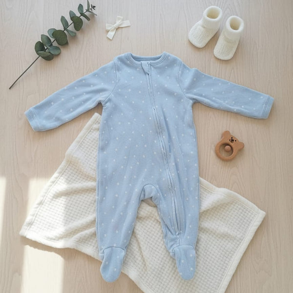 Blue baby onesie on a white blanket with baby booties and a branch on a wooden surface