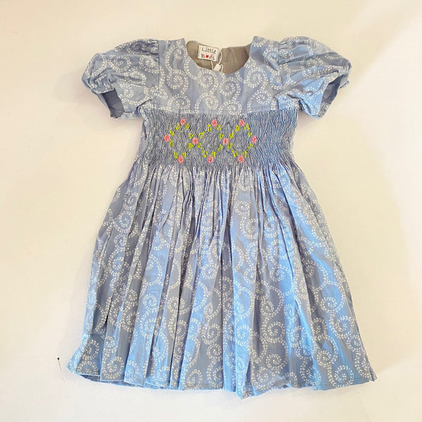 A short-sleeved blue patterned dress with smocked detailing and embroidery on the chest area for girls.
