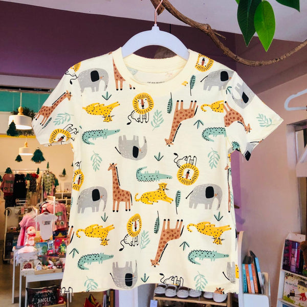 A boys' cotton t-shirt displayed on a hanger, featuring a colorful animal pattern with giraffes, lions, and a flamingo.