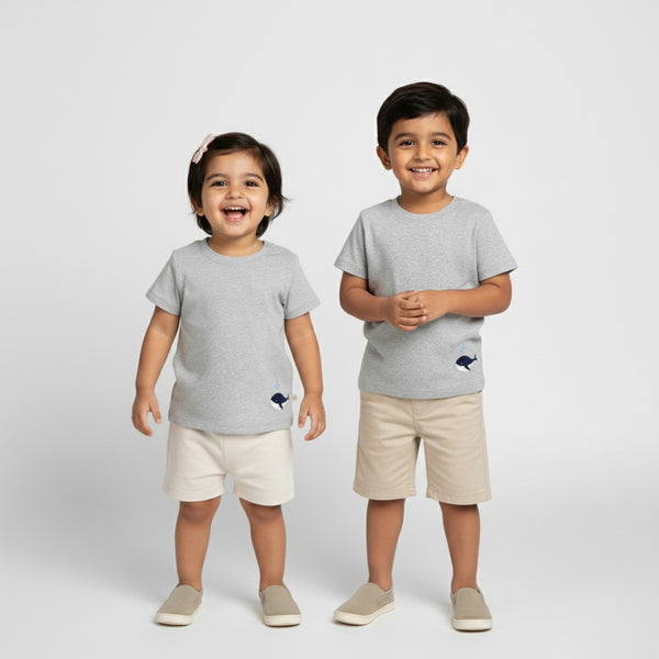 Two children wearing matching gray t-shirts and beige shorts on a white background