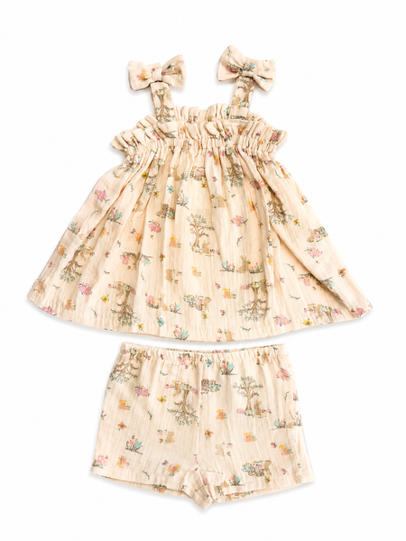 A two-piece baby girl's outfit set featuring a sleeveless ruffled dress with bow straps and matching shorts, both in a light beige gauze fabric with a delicate multicolor woodland print of deer, flowers, and trees.