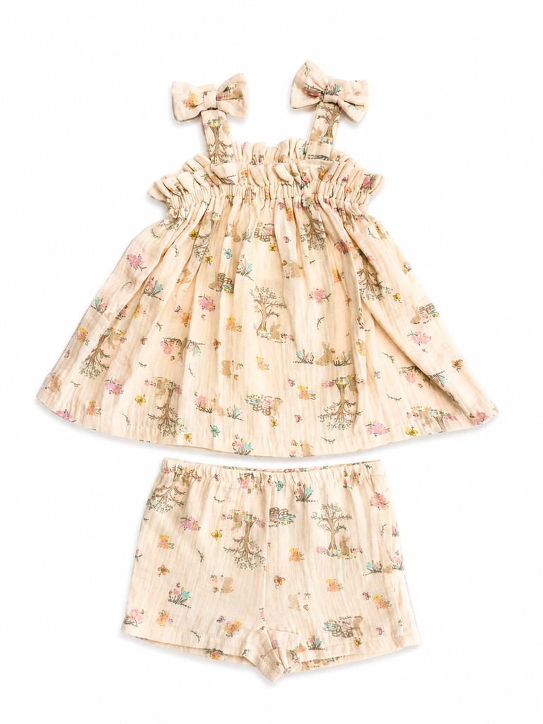 A two-piece baby girl's outfit set featuring a sleeveless ruffled dress with bow straps and matching shorts, both in a light beige gauze fabric with a delicate multicolor woodland print of deer, flowers, and trees.