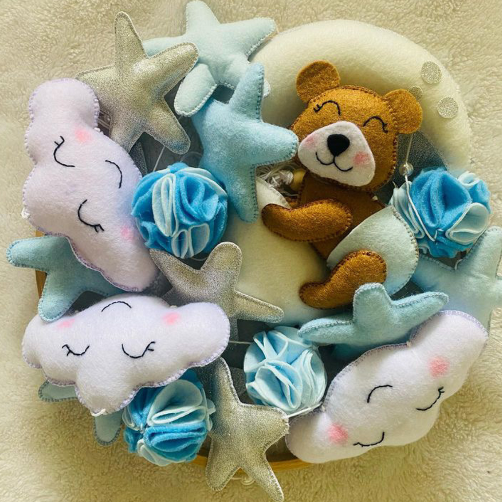 Handcrafted felt mobile with bear and cloud theme, featuring blue stars and a brown bear plush toy.