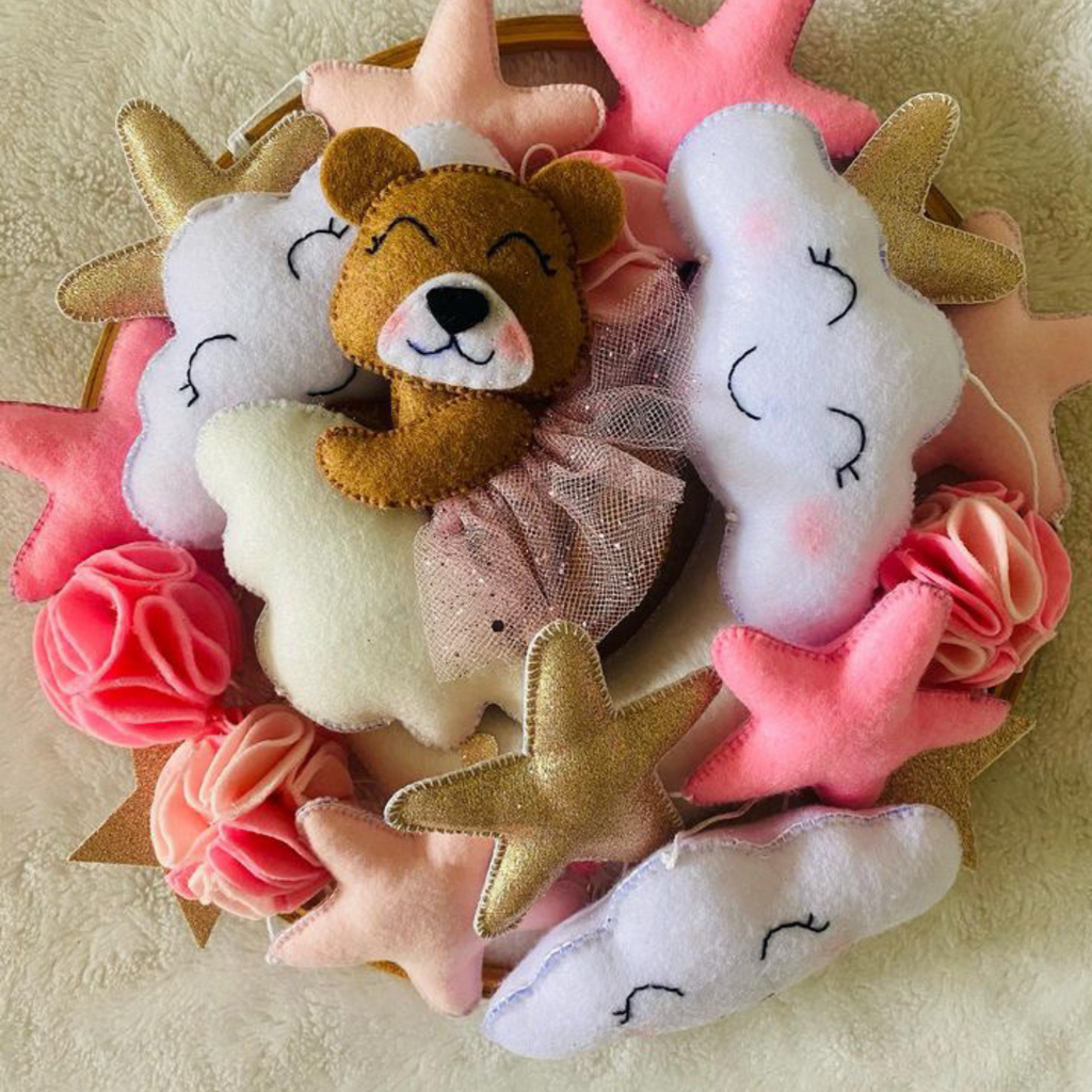 Handcrafted felt mobile with a bear and cloud theme, featuring various shades of pink and white, with a metal loop for hanging.