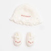 A white crochet embroidered cap and booties set for newborns with pink details.