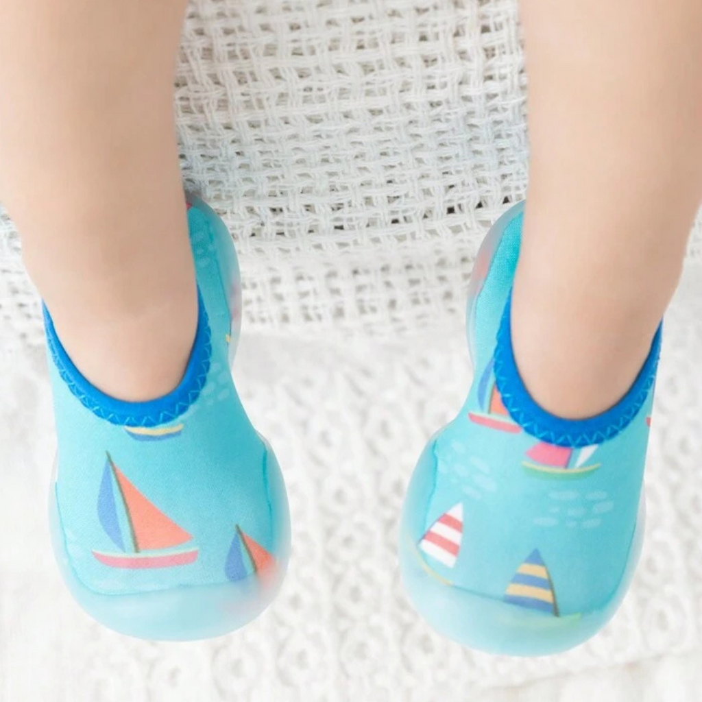 A pair of children's swim shoes with a rubber base and a sailing theme, featuring colorful sailboat patterns on a blue background.