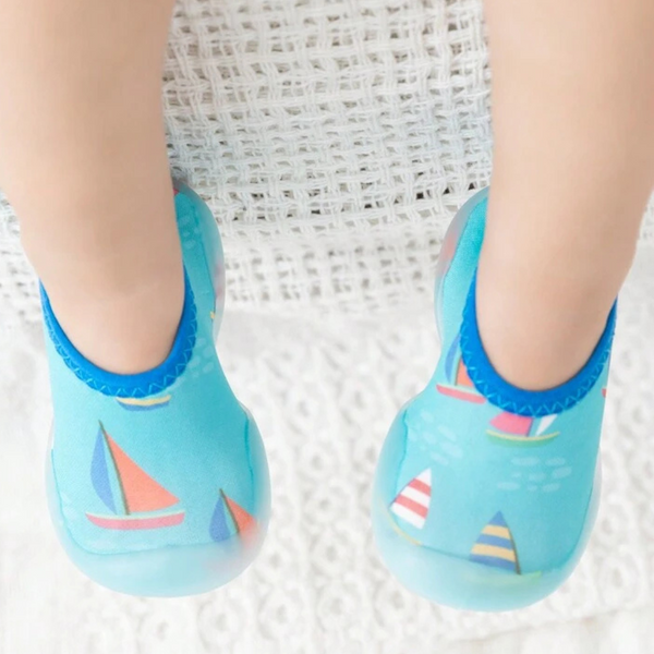 A pair of children's swim shoes with a rubber base and a sailing theme, featuring colorful sailboat patterns on a blue background.