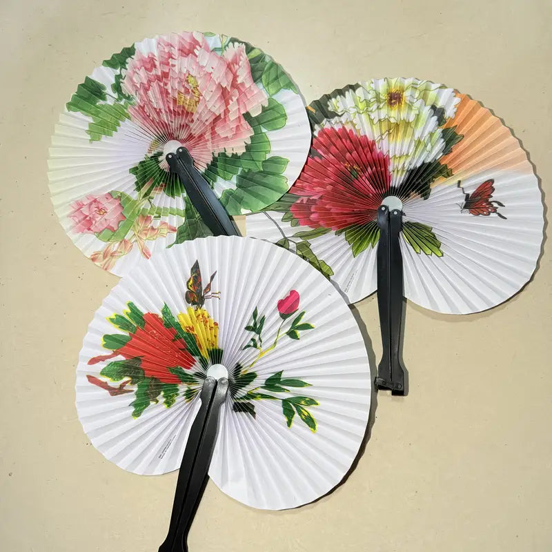 Three decorative fans with floral and butterfly designs on a beige background