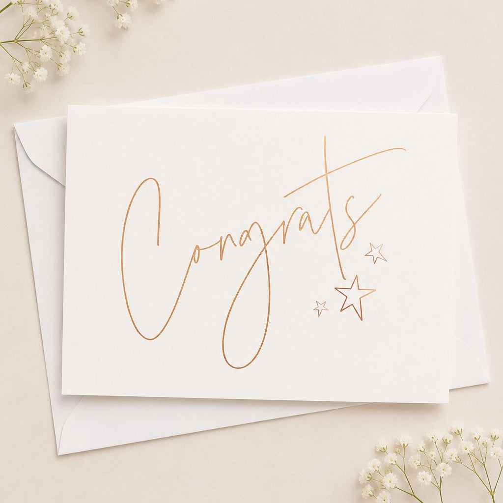 White card with 'Congrats' in rose gold script on a beige background with small white flowers.