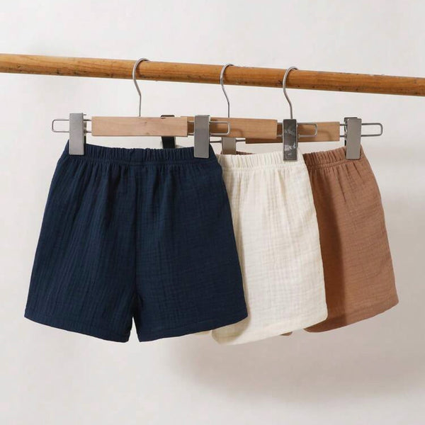 Three pairs of shorts in navy, white, and brown hanging on a rack against a light background.