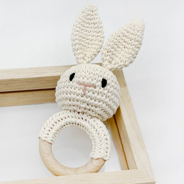 Crocheted rabbit rattle with wooden ring on a light background