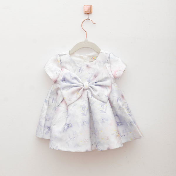 White dress with colorful floral pattern and large bow on a hanger against a white background