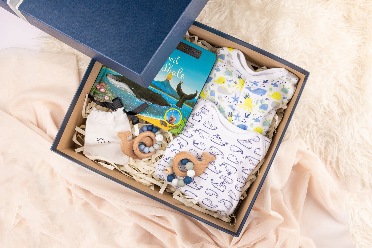Baby Gift Box with curated items consisting of a teether rattle, organic baby clothing, board book and baby accessories.