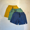 Three pairs of shorts in yellow, green, and blue on a light background